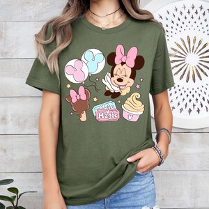 May include: A green t-shirt with a cartoon image of Minnie Mouse, balloons, a Mickey Mouse ice cream cone, and a ticket that says "Magic".