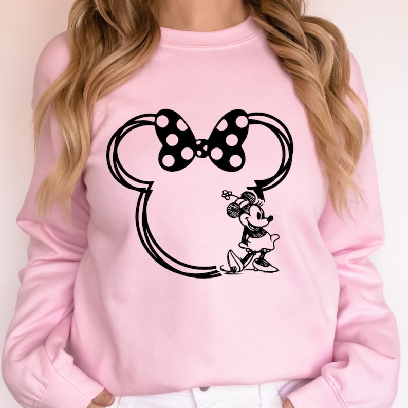 May include: A pink sweatshirt with a black and white outline of Mickey Mouse's head and Minnie Mouse standing inside the outline. Minnie Mouse is wearing a black dress with white polka dots and a black bow.