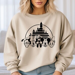 May include: A beige sweatshirt with a black graphic of Mickey Mouse, Minnie Mouse, Donald Duck, Goofy, and the iconic Cinderella's Castle.
