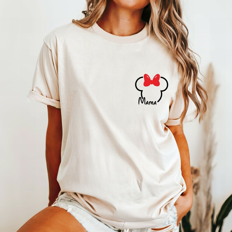 Puede incluir: Una camiseta de color crema con un gr&aacute;fico negro y rojo de una cabeza de rat&oacute;n con un lazo y la palabra "Mama" debajo.