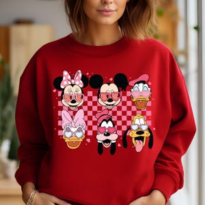 May include: Red sweatshirt with a checkered pattern and images of Mickey Mouse, Minnie Mouse, Donald Duck, Daisy Duck, Goofy, and Pluto wearing heart-shaped sunglasses.
