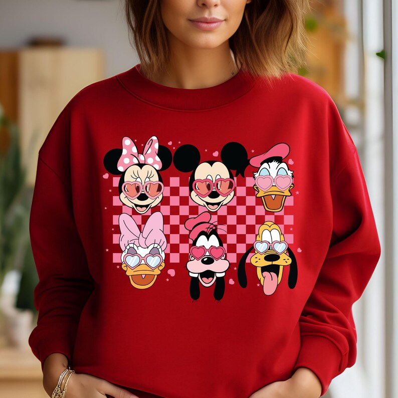 May include: Red sweatshirt with a checkered pattern and images of Mickey Mouse, Minnie Mouse, Donald Duck, Daisy Duck, Goofy, and Pluto wearing heart-shaped sunglasses.