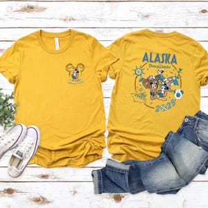 May include: Mustard yellow t-shirts with front and back graphics. The front features a Mickey Mouse design with text. The back displays "Alaska Disney Wonder 2025" with Mickey and Minnie Mouse characters and other graphics.