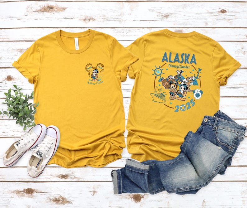 May include: Mustard yellow t-shirts with front and back graphics. The front features a Mickey Mouse design with text. The back displays "Alaska Disney Wonder 2025" with Mickey and Minnie Mouse characters and other graphics.