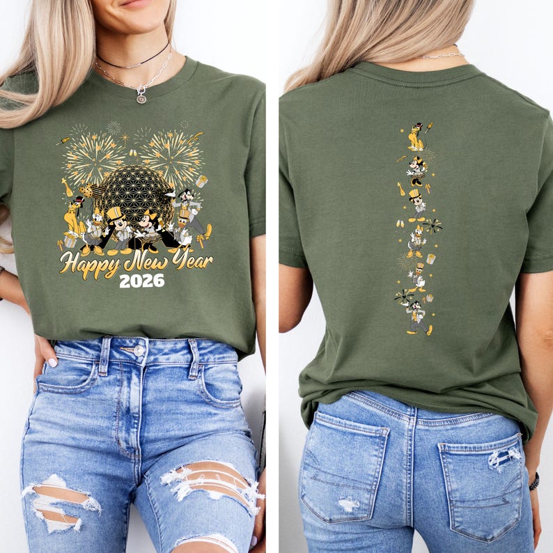 May include: Olive green t-shirt with a festive design for the New Year. The front features fireworks, a geometric sphere, and cartoon characters with the text "Happy New Year 2026." The back has a vertical line of cartoon characters. The model is wearing blue jeans.