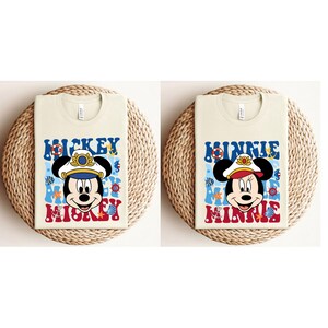 May include: Two beige t-shirts with a nautical theme. The left shirt features Mickey Mouse wearing a captain's hat and the text "Mickey Mouse". The right shirt features Minnie Mouse wearing a captain's hat and the text "Minnie Mouse".
