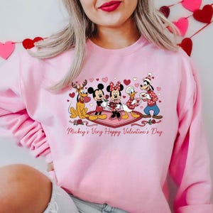 May include: Pink sweatshirt featuring Mickey Mouse, Minnie Mouse, Donald Duck, Goofy, and Pluto with Valentine's Day hearts and roses. The text "Mickey's Very Happy Valentine's Day" is printed below the characters.