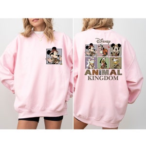 Pu&ograve; includere: Felpa rosa con una grafica di Topolino e altri personaggi Disney in abiti da safari. Il testo "Disney Animal Kingdom" &egrave; stampato sul retro.