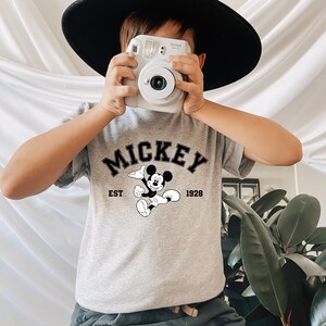 May include: A grey t-shirt with a black Mickey Mouse graphic and the text "MICKEY EST 1928".