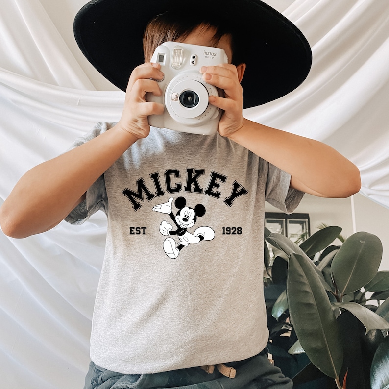 May include: A grey t-shirt with a black Mickey Mouse graphic and the text "MICKEY EST 1928".
