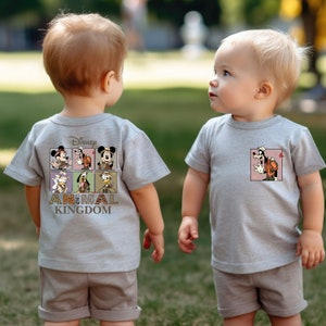 Pu&ograve; includere: Due bambini indossano magliette grigie con grafica Disney's Animal Kingdom. Una maglietta presenta un gruppo di personaggi Disney, l'altra presenta Goofy. Entrambi i bambini indossano pantaloncini color kaki.