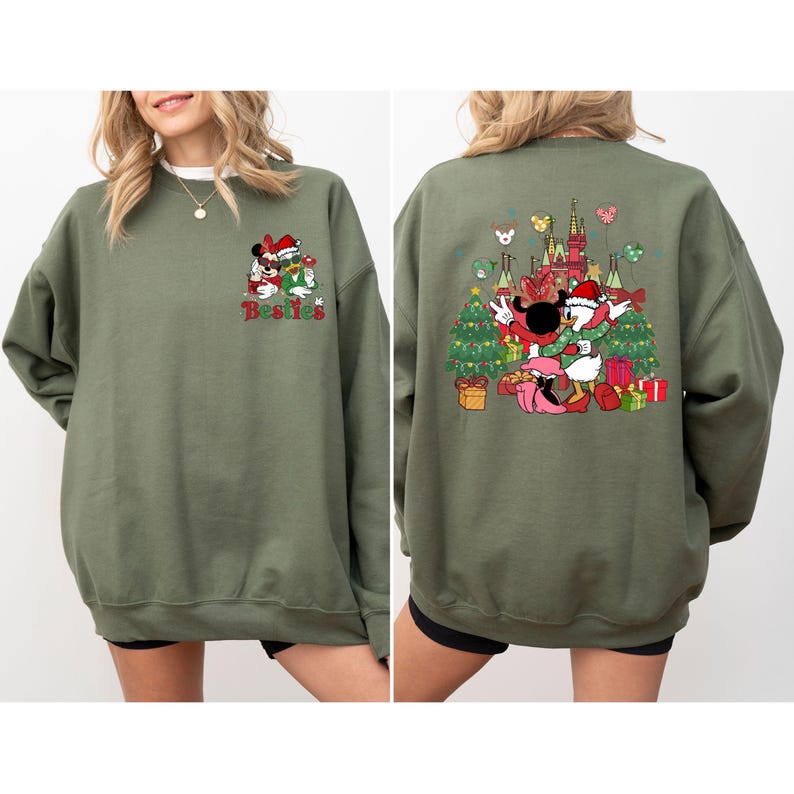 May include: An olive green sweatshirt featuring a festive design. The front displays Minnie Mouse and Mickey Mouse with the word "Besties". The back showcases Mickey and Donald Duck with a Christmas tree and castle.