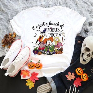 Op de afbeelding: Wit T-shirt met een afbeelding van Mickey Mouse, Goofy en Winifred Sanderson uit de film Hocus Pocus. De tekst "it's just a bunch of Hocus Pocus" staat op het T-shirt gedrukt.