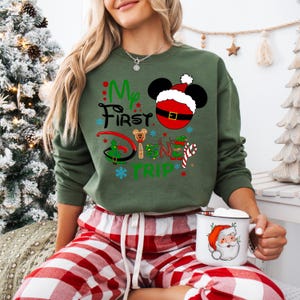 May include: Green Christmas themed sweatshirt with the text "My First Disney Trip" and a Mickey Mouse head wearing a Santa hat.