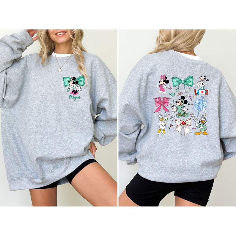 May include: A light gray sweatshirt featuring a cartoon design of Minnie Mouse and other Disney characters. The front has a teal bow and the name "Megan". The back has multiple bows and characters. The sweatshirt has a white collar.