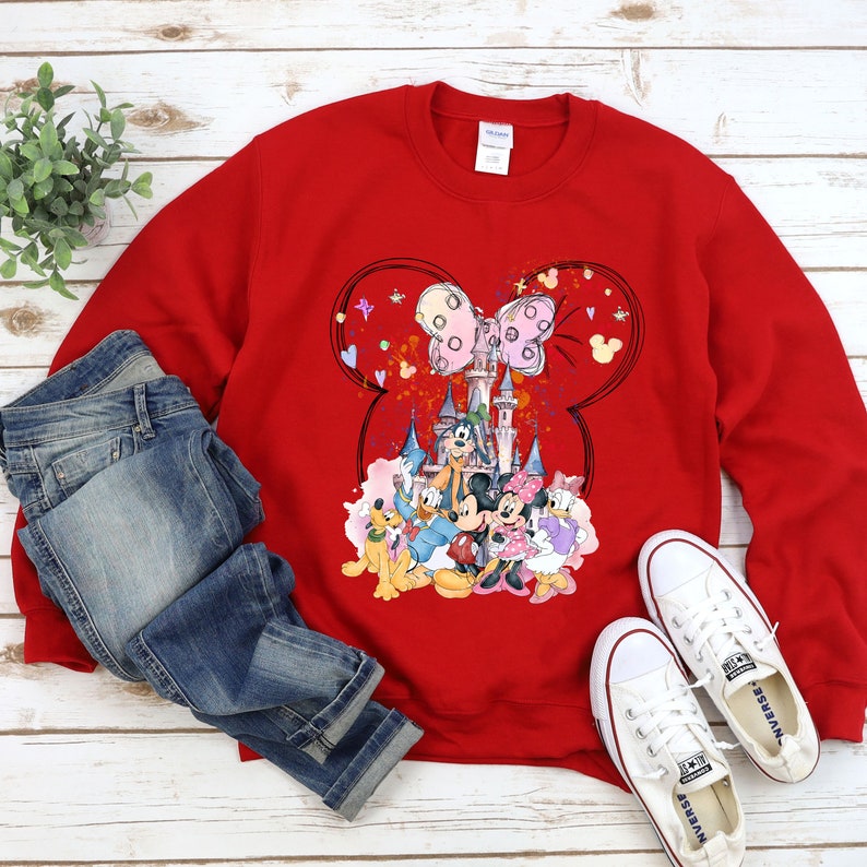 May include: Red sweatshirt with a graphic print of Mickey Mouse and friends in front of the Disney castle. The graphic also includes Minnie Mouse's iconic bow and hearts.