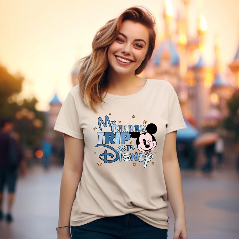 Puede incluir: Una camiseta blanca con un gr&aacute;fico azul y blanco que dice "My Christmas Trip to Disney" con una cabeza de Mickey Mouse de dibujos animados. El gr&aacute;fico tambi&eacute;n incluye estrellas amarillas.