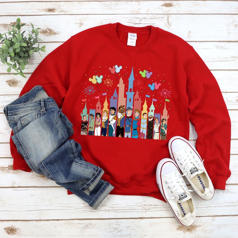 Puede incluir: Sudadera roja con un gr&aacute;fico de un castillo de Disney y varios pr&iacute;ncipes de Disney. El castillo est&aacute; rodeado de globos y fuegos artificiales de colores.