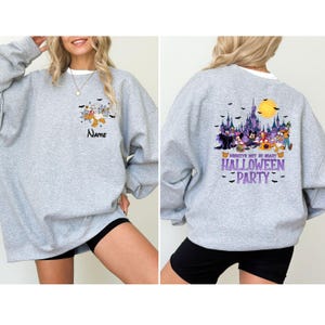 May include: A light gray sweatshirt with a Halloween-themed design. The front features a cartoon graphic and the word "Name". The back displays a colorful graphic of Disney characters, a castle, and the text "Mickey's Not So Scary Halloween Party".