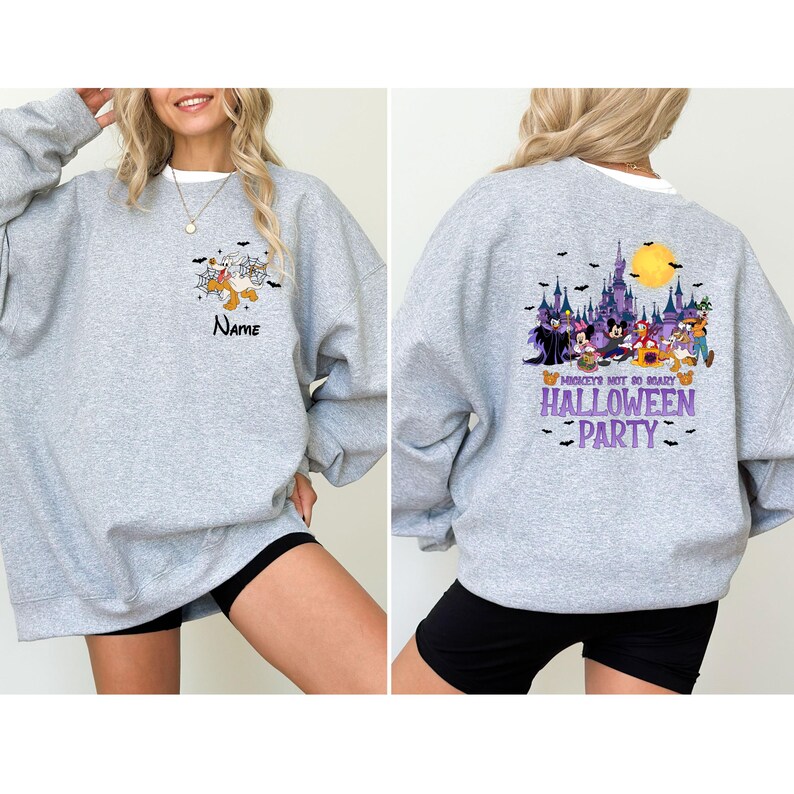 May include: A light gray sweatshirt with a Halloween-themed design. The front features a cartoon graphic and the word "Name". The back displays a colorful graphic of Disney characters, a castle, and the text "Mickey's Not So Scary Halloween Party".