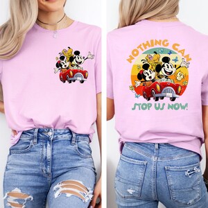 May include: Pink t-shirt with a vintage-style graphic of Mickey Mouse, Minnie Mouse, and Pluto driving a red car on the front. The back of the shirt has a graphic of Mickey Mouse, Minnie Mouse, and Pluto driving a red car with the text "Nothing Can Stop Us Now!" in a retro font.