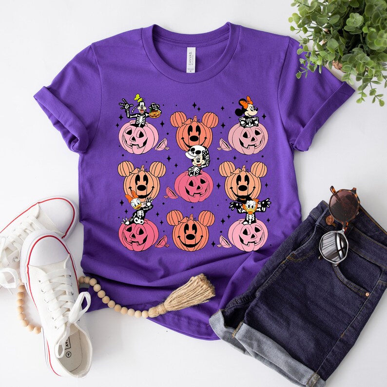May include: Purple t-shirt with a Halloween design featuring Mickey Mouse, Minnie Mouse, Donald Duck, and Goofy characters inside pumpkins.