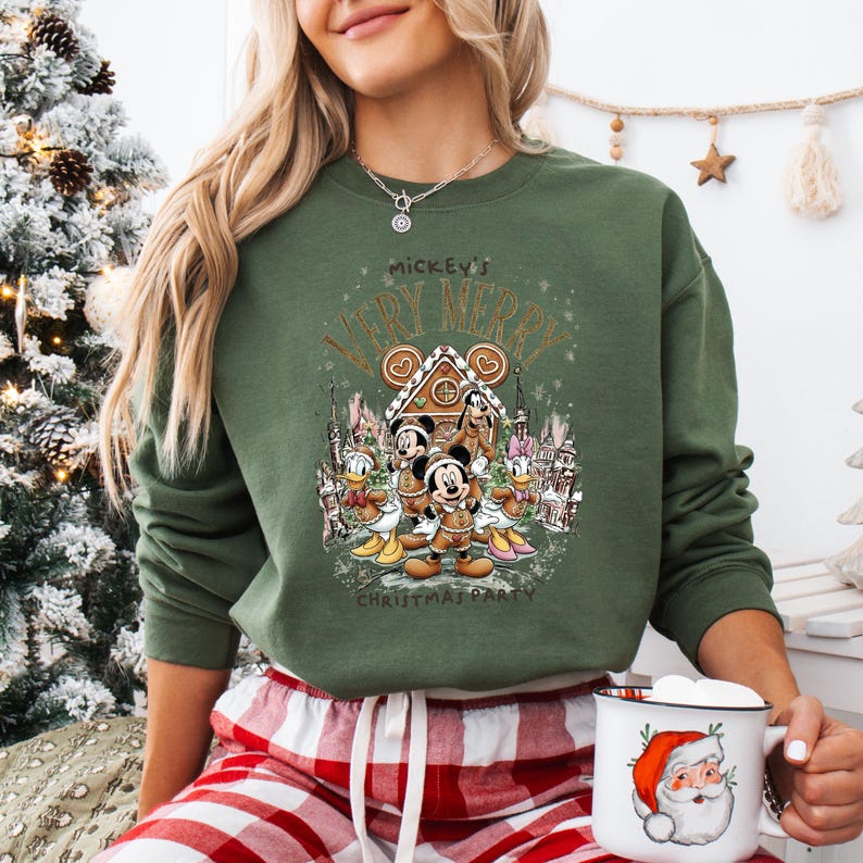 Puede incluir: Sudadera verde con un dise&ntilde;o festivo de Mickey Mouse y sus amigos. El dise&ntilde;o incluye una casa de jengibre y el texto "Mickey's Very Merry Christmas Party". La sudadera se combina con un pantal&oacute;n de pijama a cuadros rojos y blancos.