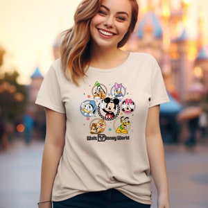 Op de afbeelding: Een beige T-shirt met een kleurrijke afbeelding van Mickey Mouse en zijn vrienden in cirkels. De tekst "Walt Disney World" staat onder de afbeelding.