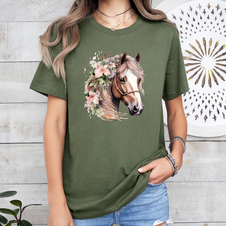 Peut inclure: T-shirt vert olive avec une illustration &agrave; l'aquarelle d'une t&ecirc;te de cheval orn&eacute;e de fleurs roses. Le cheval a une crini&egrave;re brune et un licol. Le t-shirt est de style d&eacute;contract&eacute;.