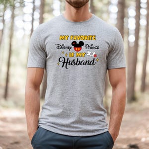 May include: A gray t-shirt with the text "MY FAVORITE Disney Prince IS MY Husband" in yellow, black, red, and white. The design includes a Mickey Mouse head and white gloves.