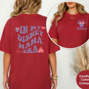 Puede incluir: Camiseta de color rojo carmes&iacute; con el texto "IN MY DISNEY MAMA ERA" en morado y rosa. La parte trasera de la camiseta presenta un gr&aacute;fico de castillo. La parte delantera de la camiseta tiene un logotipo de Disney Mama y el nombre "Emma".