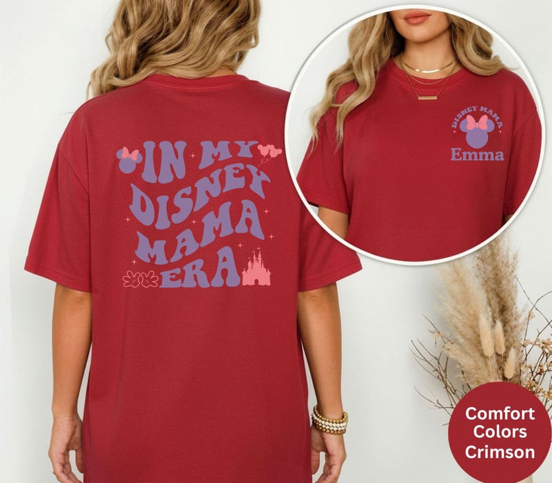 Puede incluir: Camiseta de color rojo carmes&iacute; con el texto "IN MY DISNEY MAMA ERA" en morado y rosa. La parte trasera de la camiseta presenta un gr&aacute;fico de castillo. La parte delantera de la camiseta tiene un logotipo de Disney Mama y el nombre "Emma".