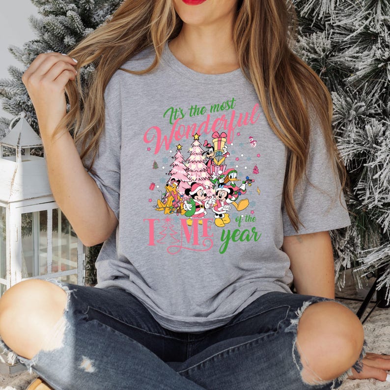 May include: A gray t-shirt with a pink and green graphic of Mickey Mouse and friends celebrating Christmas. The text on the shirt reads "It's the most wonderful time of the year."