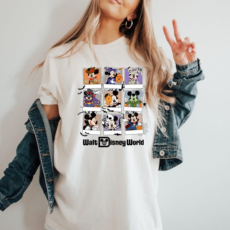 Op de afbeelding: Wit T-shirt met een afbeelding van Mickey Mouse en zijn vrienden verkleed in Halloween-kostuums. De afbeelding is gerangschikt in een raster van negen vierkanten, waarbij elk vierkant een ander personage toont. De tekst "Walt Disney World" staat onder de afbeelding.