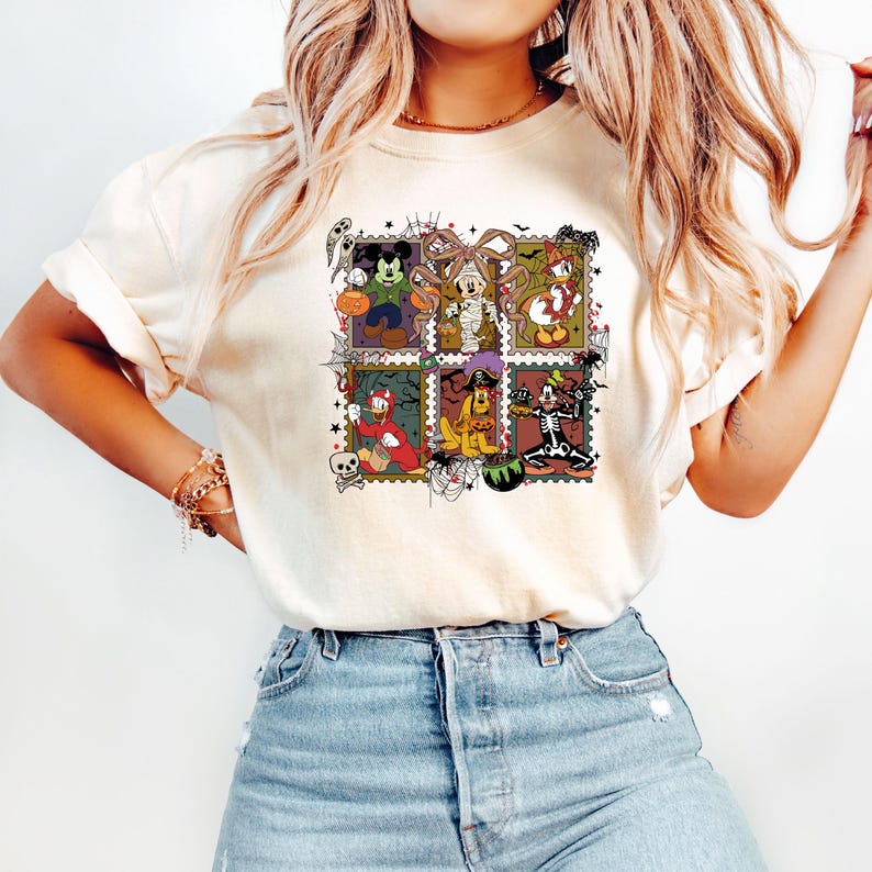 以下が含まれることがあります： クリーム色のTシャツ。ハロウィーンをテーマにしたカラフルなグラフィックが特徴です。グラフィックは、ハロウィーンのコスチュームを着た様々な漫画のキャラクターをグリッドパターンで表示しています。デザインには、幽霊、カボチャ、クモの巣が含まれています。