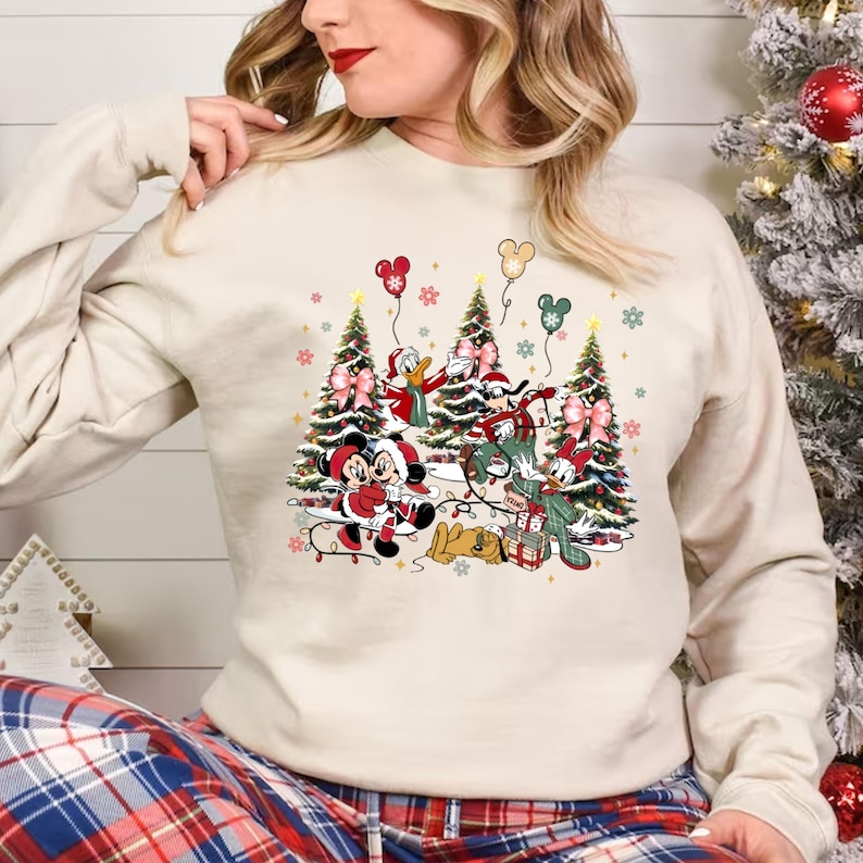 May include: A cream-colored sweatshirt with a Christmas-themed design featuring Mickey Mouse, Minnie Mouse, Donald Duck, Goofy, and Pluto. The characters are standing in front of decorated Christmas trees with presents and lights.