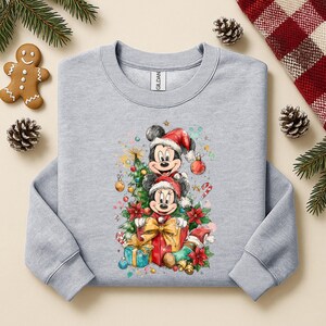 May include: A light gray sweatshirt featuring a festive Christmas design with Mickey and Minnie Mouse wearing Santa hats. The graphic includes a Christmas tree, presents, and candy canes, perfect for holiday wear.
