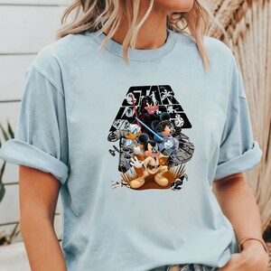 May include: Light blue t-shirt with a graphic print of Mickey Mouse, Donald Duck, and Goofy dressed as Star Wars characters. The graphic includes the text "Star Wars" in black.