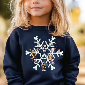 May include: A navy blue sweatshirt with a white snowflake design featuring various Disney characters wearing Santa hats. The characters include Mickey Mouse, Minnie Mouse, Donald Duck, Goofy, Pluto, and others. The snowflake design also includes a silhouette of the Cinderella Castle.
