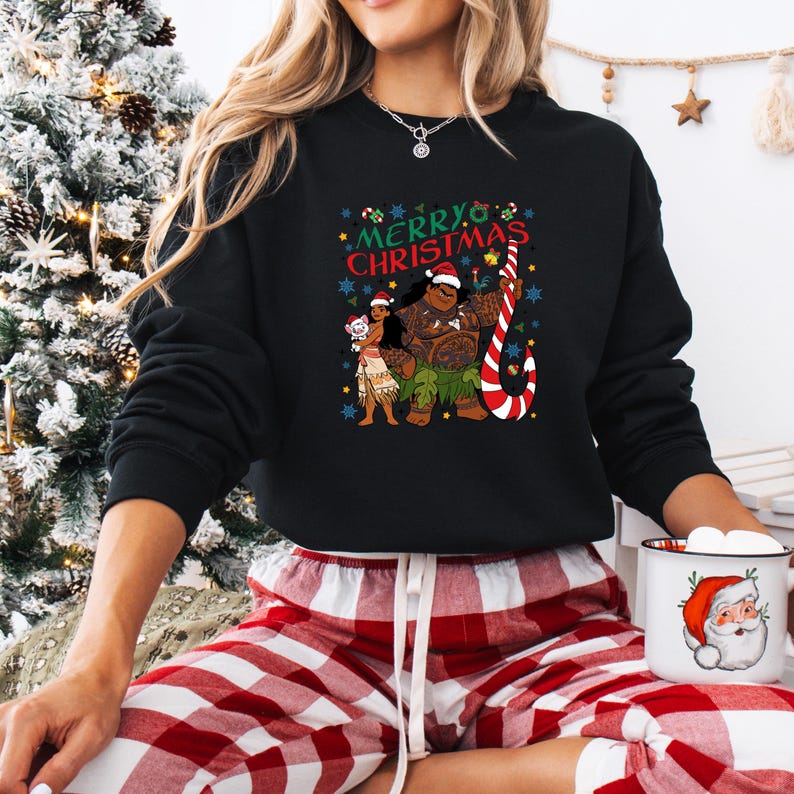 May include: Black sweatshirt featuring a festive "Merry Christmas" design with cartoon characters wearing Santa hats and holding a candy cane. The design includes a woman, a large man, and a small character. The sweatshirt is paired with red and white plaid pajama pants.