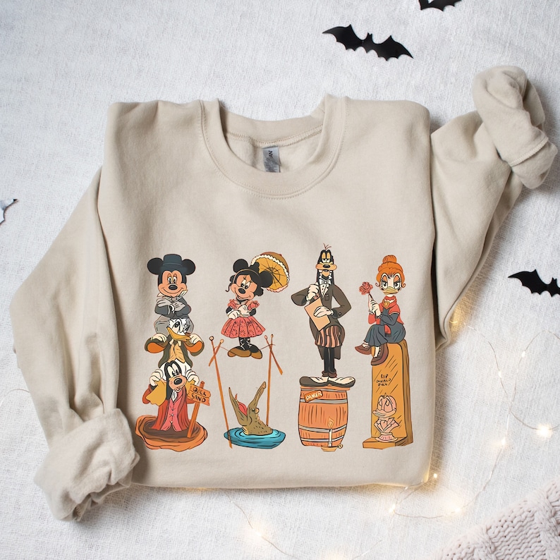 May include: A beige sweatshirt featuring a vintage-style print of Mickey Mouse, Minnie Mouse, Goofy, Donald Duck, and Pluto. The characters are dressed in various costumes and are standing on different platforms.
