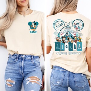 May include: A light beige t-shirt with a Mickey Mouse graphic on the front and a larger graphic on the back. The back graphic features Mickey Mouse and other Disney characters on a cruise ship with the text "2025 Alaska Disney Wonder".