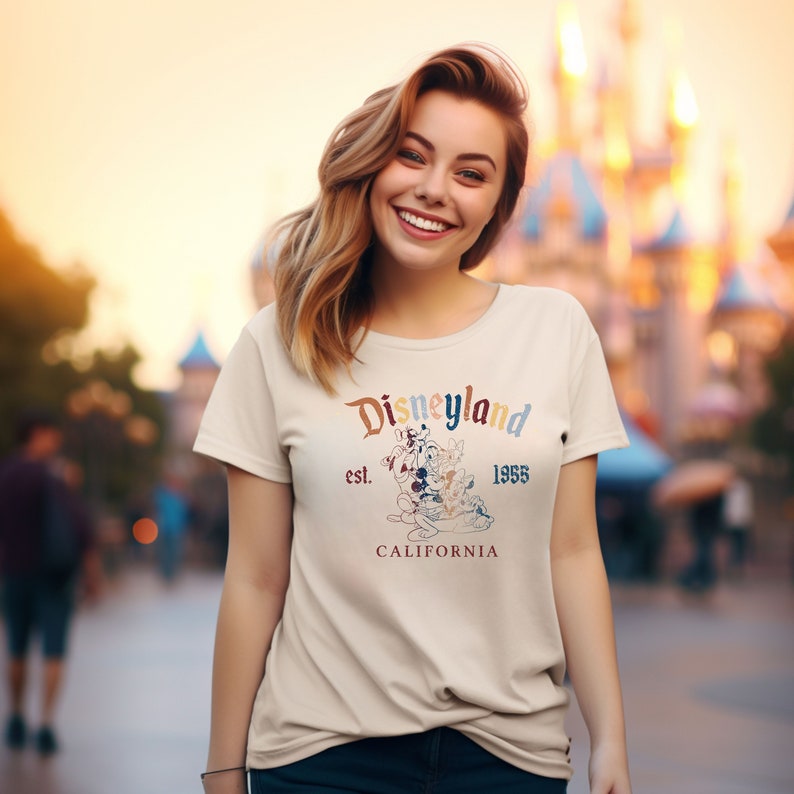 May include: A white t-shirt with a vintage-style Disneyland logo featuring Mickey Mouse, Pluto, Goofy, and Donald Duck. The logo is in rainbow colors and says "Disneyland est. 1955 California".
