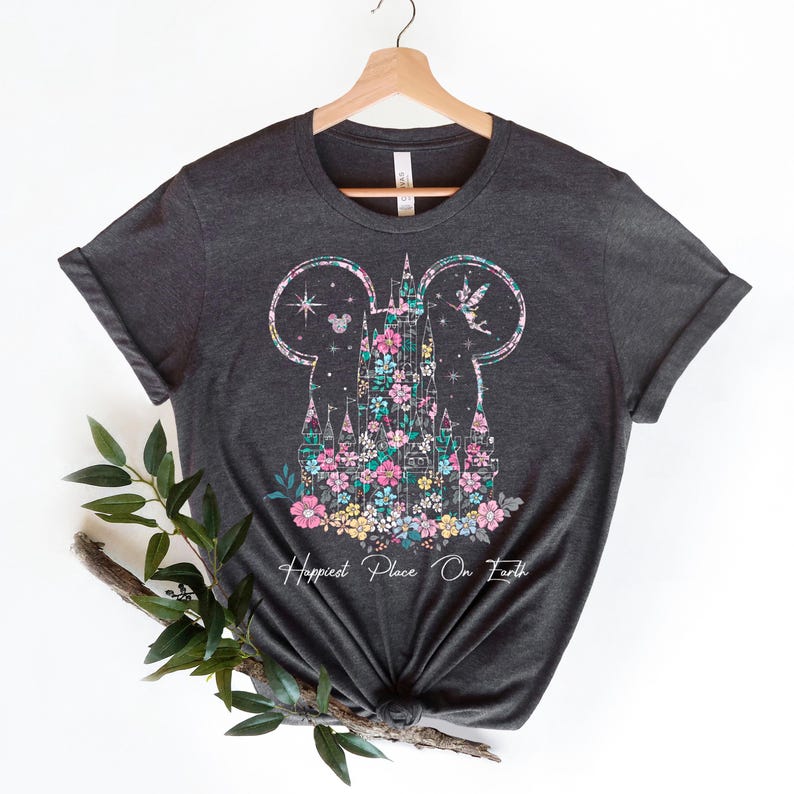 May include: A dark grey t-shirt with a floral design of Cinderella's castle in the shape of Mickey Mouse ears. The text "Happiest Place On Earth" is printed below the design.