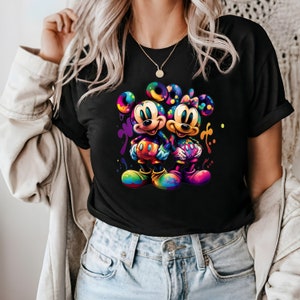 May include: Black t-shirt with a colorful graphic of Mickey Mouse and Minnie Mouse holding hands. The graphic is surrounded by colorful paint splatters.
