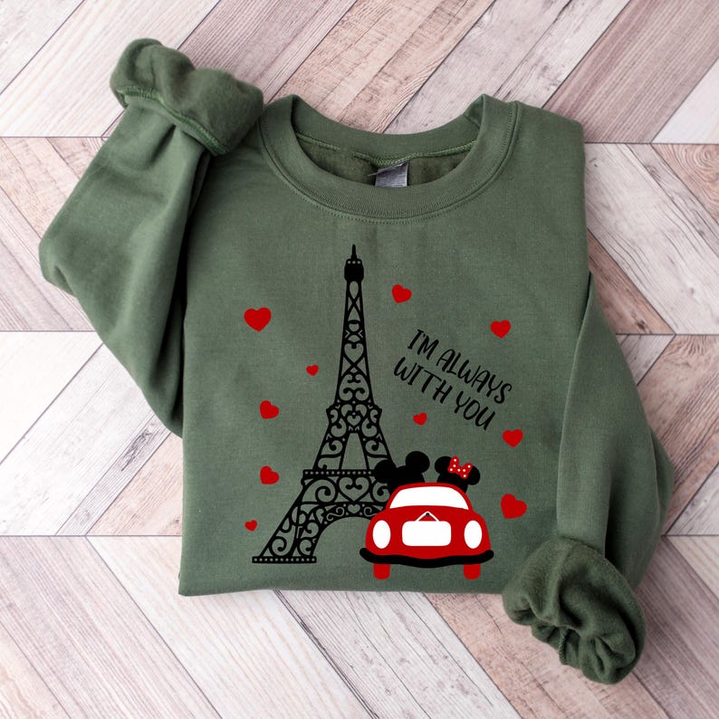May include: Green sweatshirt with a black and white graphic of the Eiffel Tower, a red car, and two cartoon figures. The text "I'm always with you" is printed on the sweatshirt.