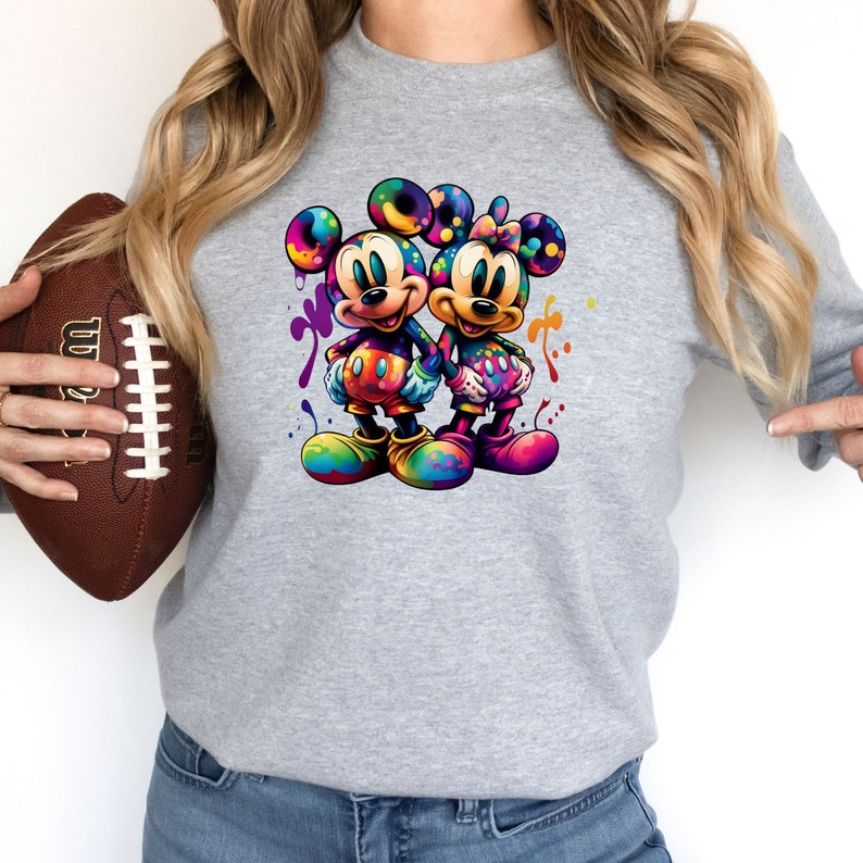May include: A gray sweatshirt with a colorful graphic of Mickey Mouse and Minnie Mouse holding hands. The graphic is surrounded by colorful paint splatters.