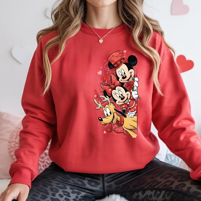 Puede incluir: Una sudadera roja con un gr&aacute;fico de Mickey y Minnie Mouse, y Pluto, con atuendos de San Valent&iacute;n. Mickey Mouse lleva un sombrero de copa, Minnie Mouse tiene un lazo y Pluto tiene alas de &aacute;ngel. Tambi&eacute;n se presentan corazones y rosas.