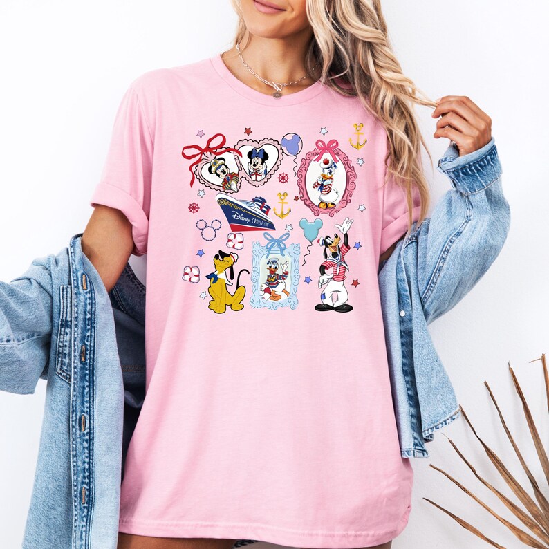 Puede incluir: Camiseta rosa con un estampado gr&aacute;fico colorido de personajes de Disney, incluyendo Mickey Mouse, Minnie Mouse, Donald Duck, Goofy y Pluto. El gr&aacute;fico tambi&eacute;n incluye un crucero y un coraz&oacute;n con el texto "Disney Cruise Line".