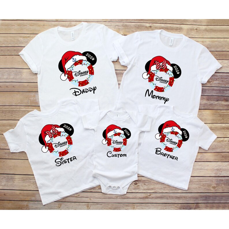 K&ouml;nnte beinhalten: Wei&szlig;e T-Shirts und ein Body mit einem Disney Cruise-Design. Jedes Shirt hat Mickey Mouse Ohren, einen Weihnachtsmannhut und das Jahr 2026. Die Shirts sind mit "Daddy", "Mommy", "Sister", "Brother" und "Custom" beschriftet.